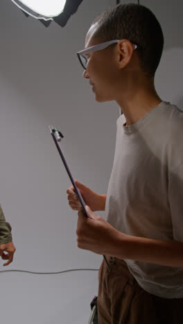 Vertical-Video-Of-Film-Director-Talking-With-Male-And-Female-Actors-Holding-Scripts-Rehearsing-For-Shooting-Movie-Or-Video-In-Studio-7